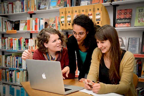 Drei junge Bildungsreferent*innen und Multiplikator*innen vor einem Laptop, diskutieren über entwicklungspolitische Themen.